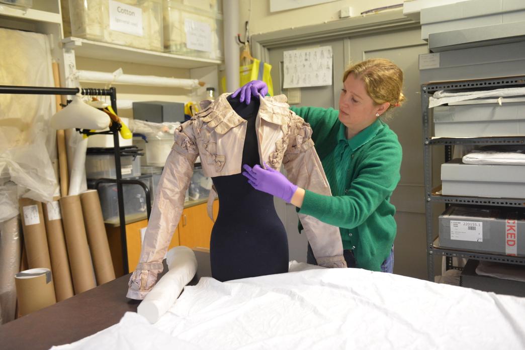 Conservator Sophie Lane carefully places a 200-year-old silk Spencer jacket on a mannequin